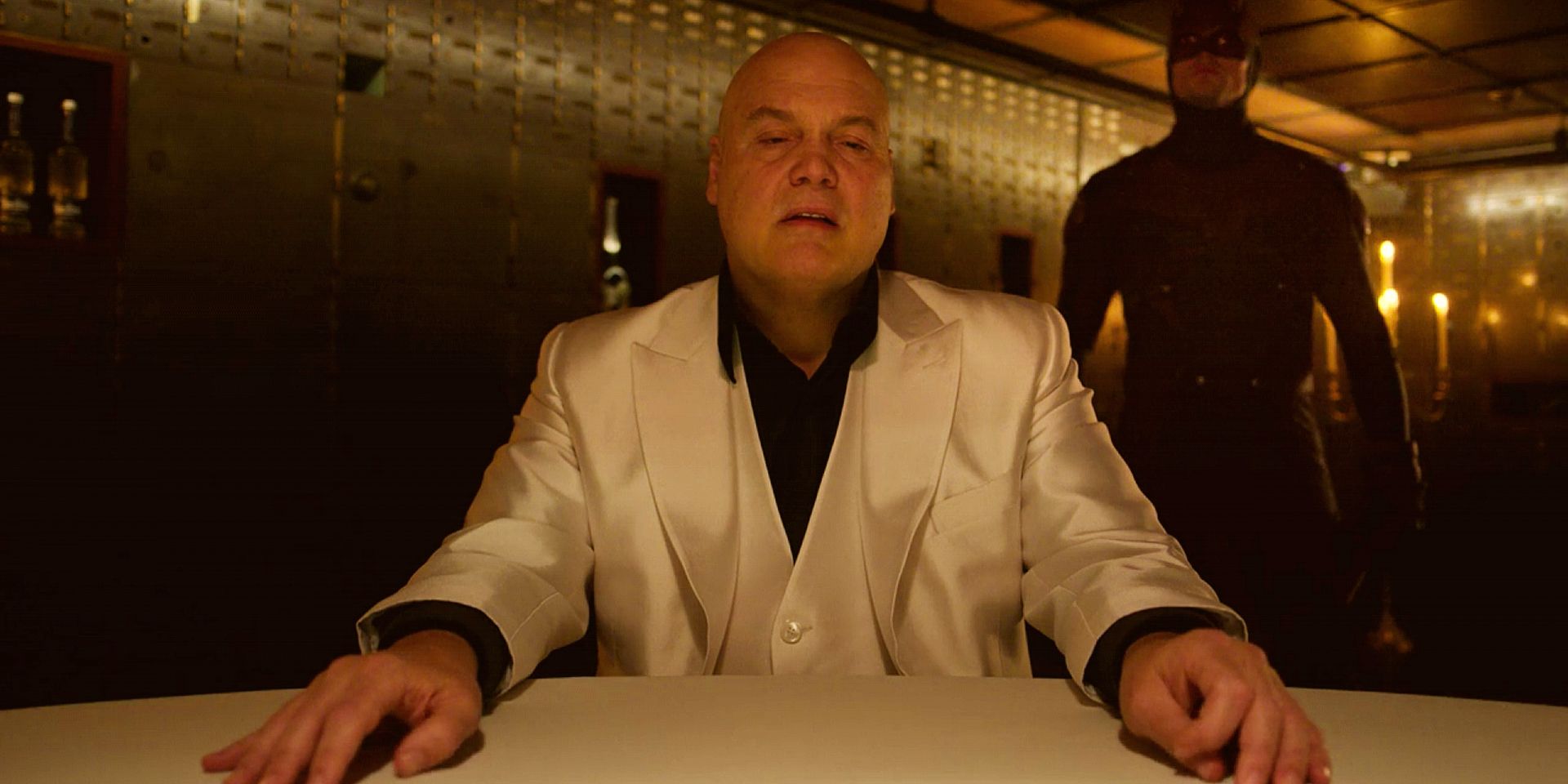 Vincent D’Onofrio in character as Kingpin, seated at a table with his hands outstretched and a snarl on his face