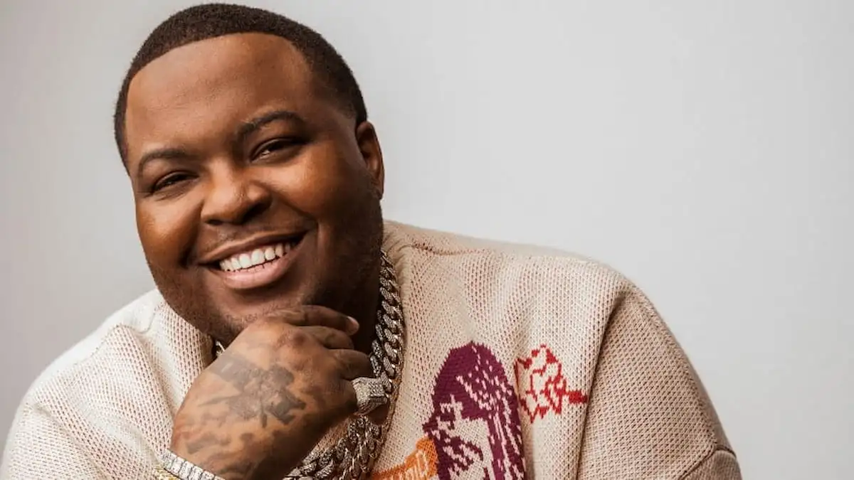 Sean Kingston has his hand on his chin and is smiling.