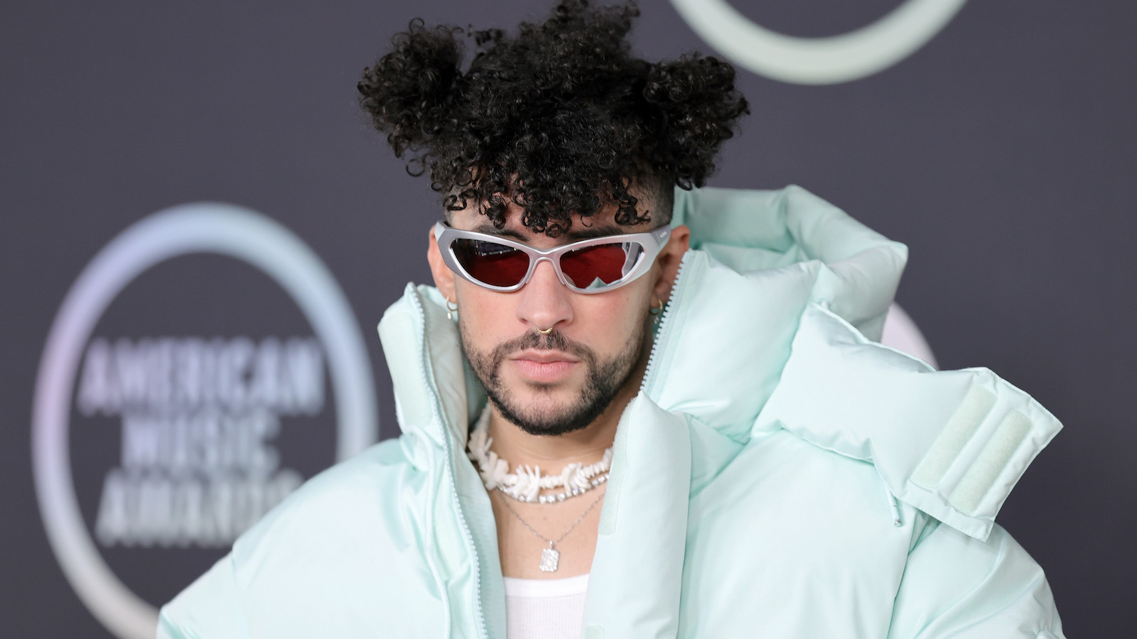 Bad Bunny is wearing sunglasses and a puffer jacket on the red carpet.