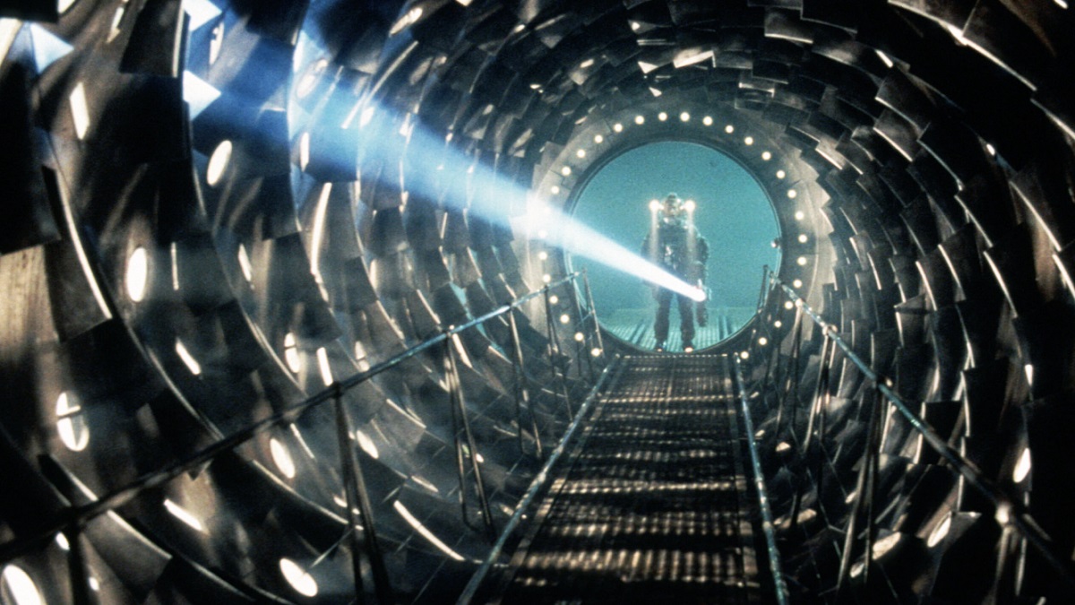 A figure in a spacesuit shines a flashlight into a circular tunnel in a still from “Event Horizon”