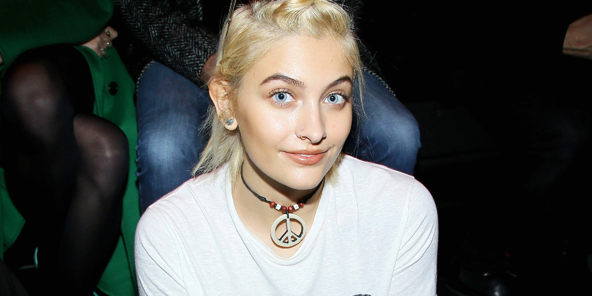 Paris Jackson is seen wearing a peace sign necklace and smiling. 