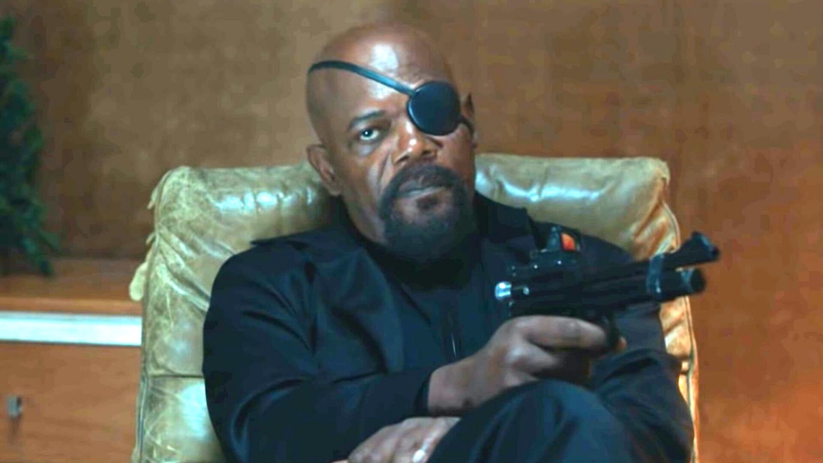 Nick Fury sitting on a couch holding a gun in a scene from Spider-Man: Far From Home