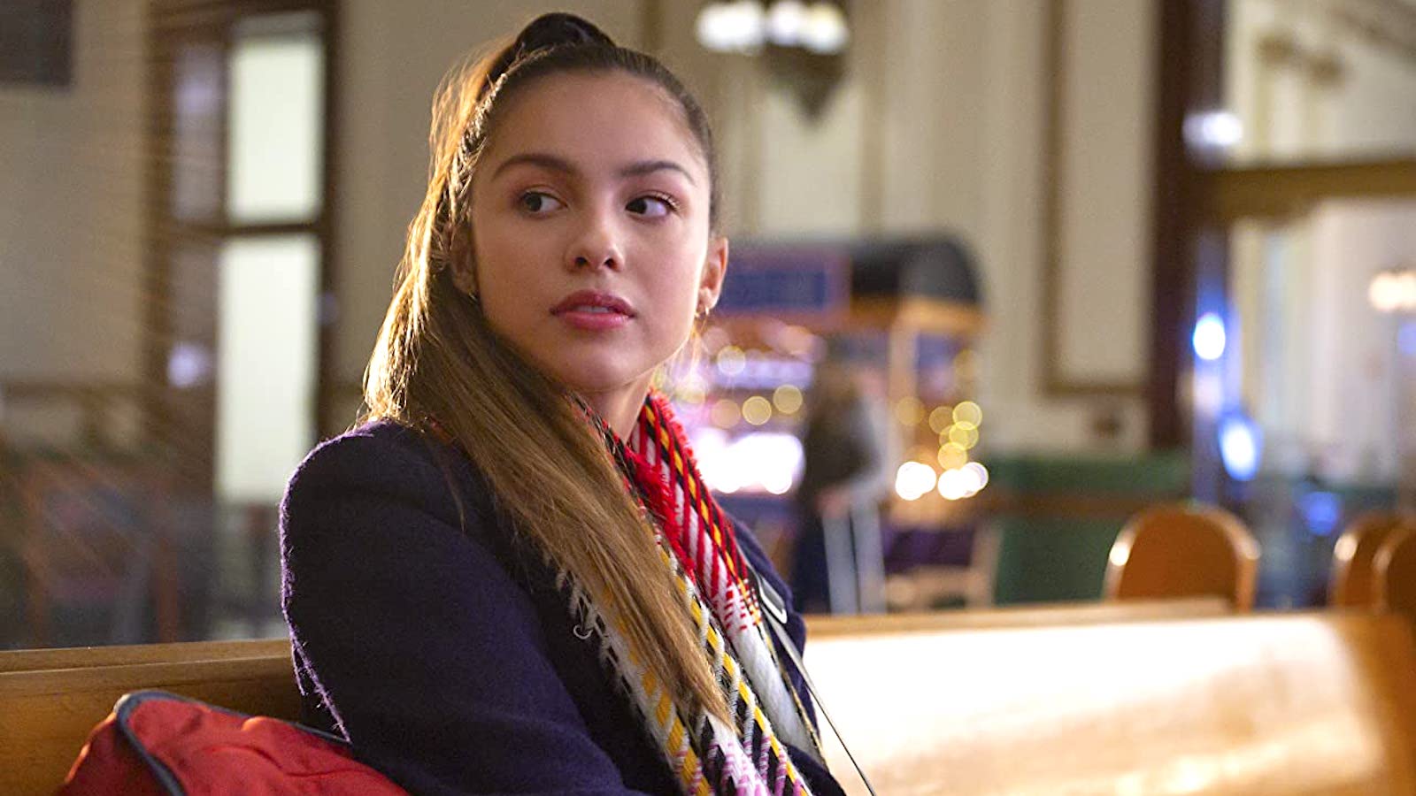 Olivia Rodrigo's Niini sitting on a bench and looking over her shoulder in 'HSMTMSM'