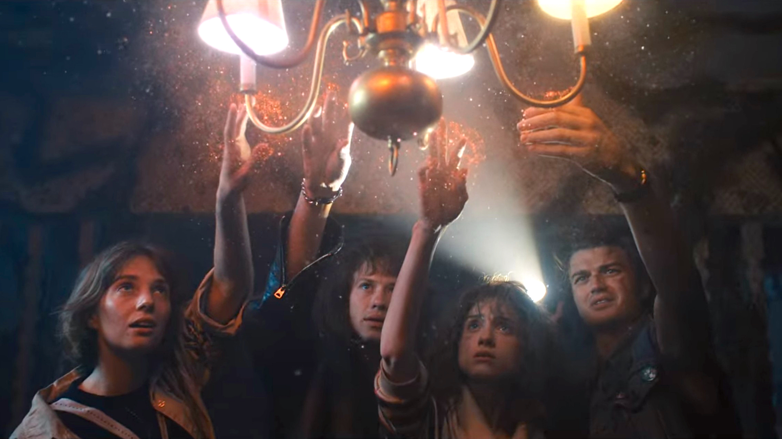 Robin, Eddie, Nancy and Mike from Stranger Things reach for a burning chandelier that's emitting glittering dust