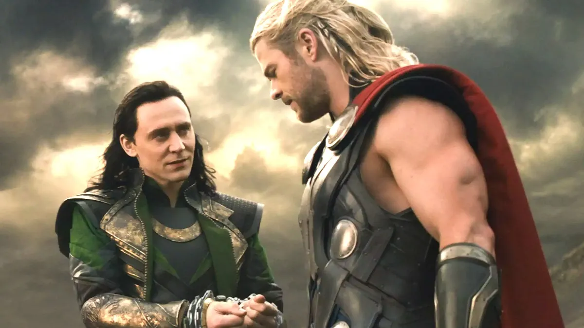 Loki and Thor are talking to each other in front of a dark and cloudy sky.