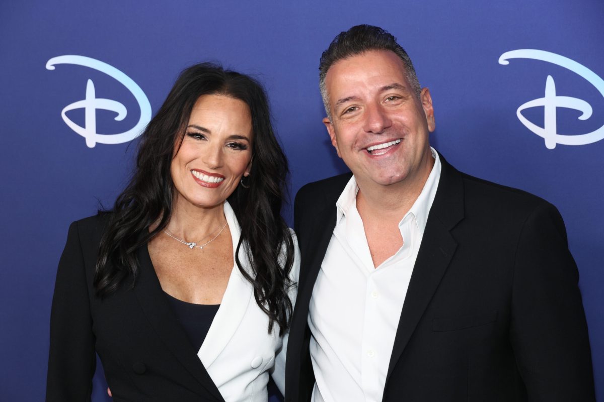 A white woman in a black and white dress (Heidi D'Amelio) and a white man in a black suit jacket with a white shirt. They're both smiling at the camera.