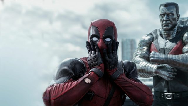 Deadpool facing the camera, covering his mouth with his hands as if in shock