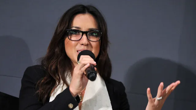 Michelle Branch is shown from the shoulders up, wearing glasses and speaking animatedly into a microphone