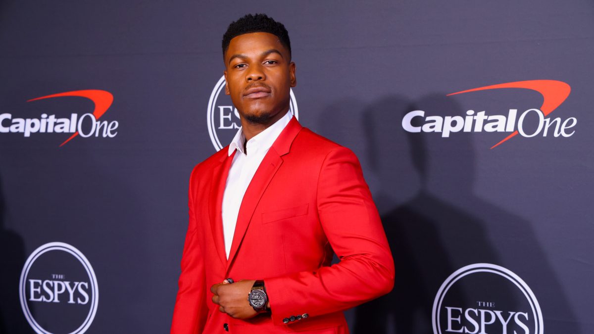 John Boyega poses for a photo in a vivid red jacket and collared white shirt