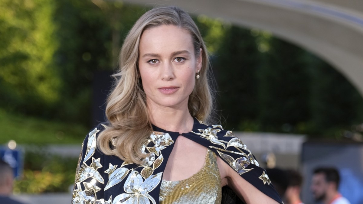 Brie Larson strikes a pose in a gold gown in front of Disneyland's Avengers Campus.