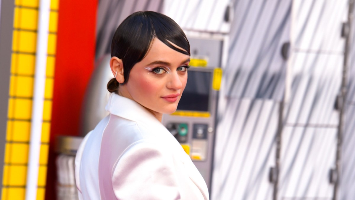 Joey King at the premiere for “Bullet Train,” wearing a white jacket, looking back over her shoulder.