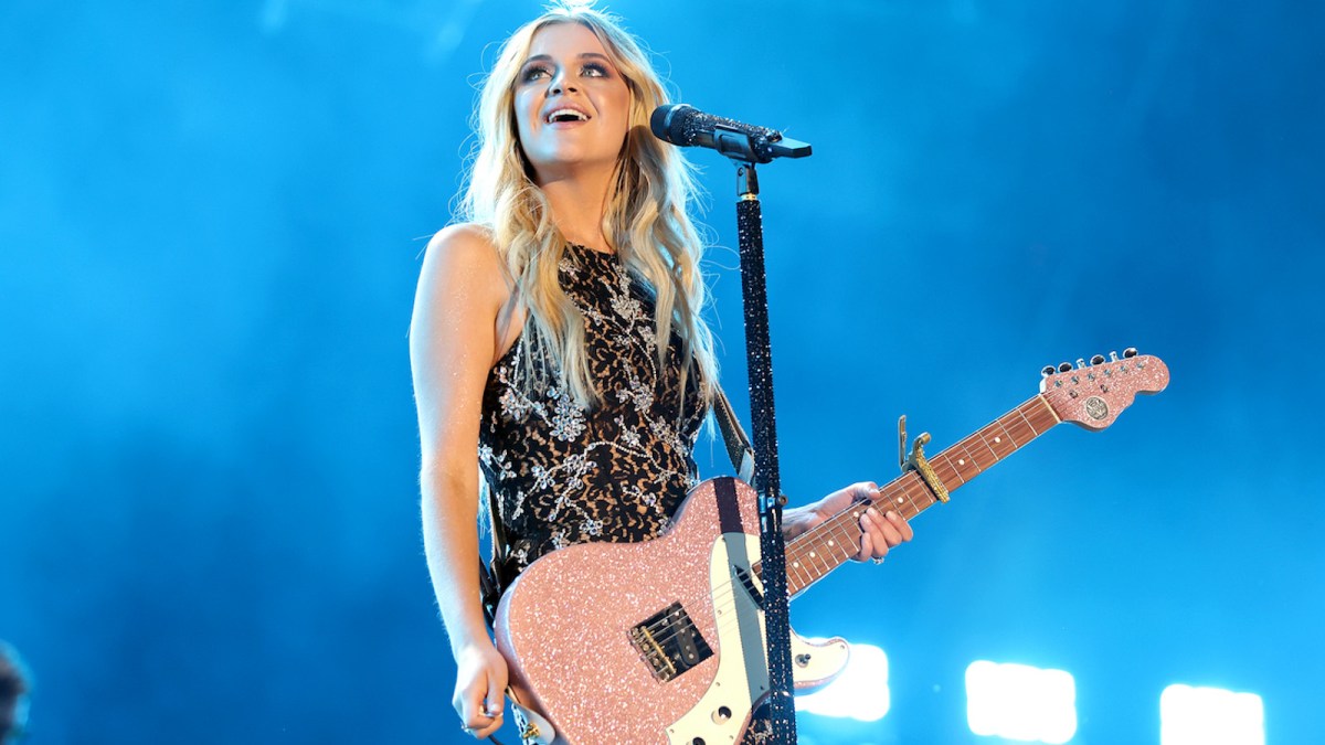 Kelsea Ballerini on stage with a mic stand and a guitar