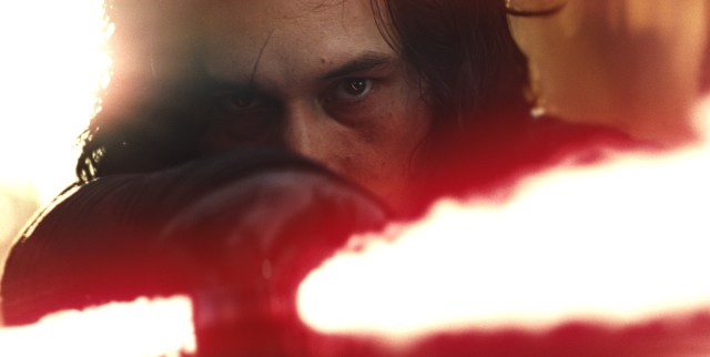 Adam Driver in character as Kylo Ren, scowling from behind the glare of his lightsaber