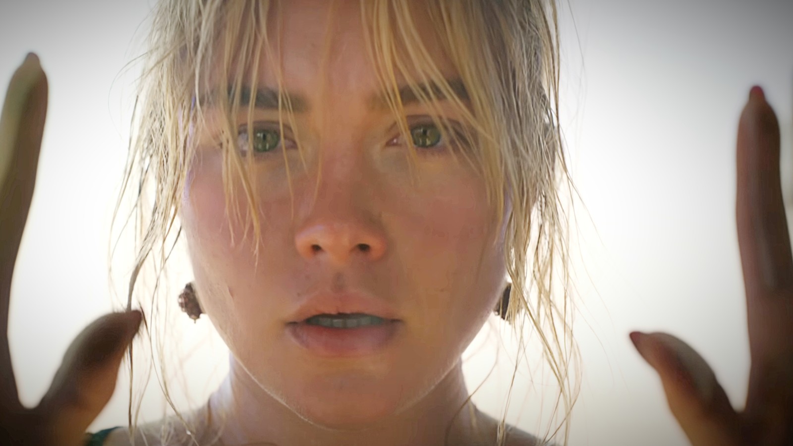 A still image of Florence Pugh's face in character from 'Don't Worry Darling' with her hands framing her face, showing a shocked expression.