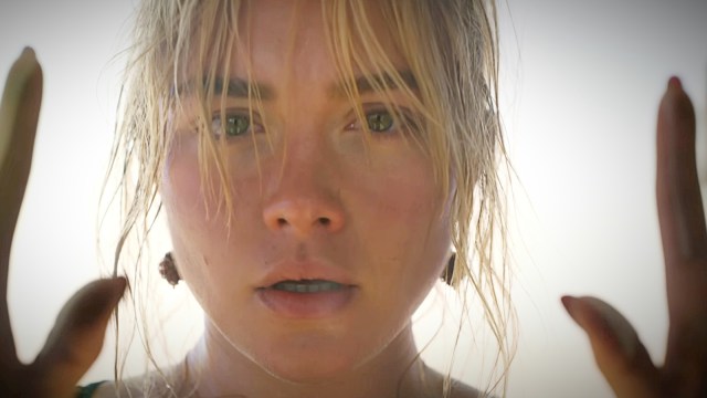 A still image of Florence Pugh’s face in character in ‘Don’t Worry Darling’ with her hands framing her face, which bears a shocked expression