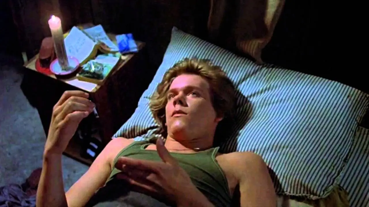 Kevin Bacon in character in a still from “Friday the 13th,” lying on his back on his camp bunk