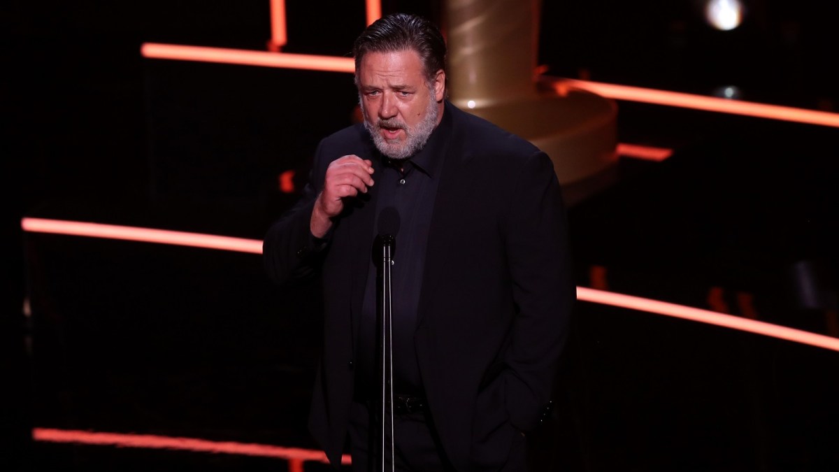 Russell Crowe sports a dapper black outfit while speaking at an award show.