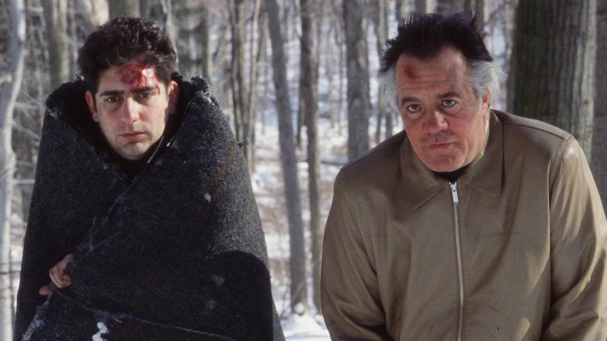 Two characters from The Sopranos stand next to each other in the woods, cold and injured.  