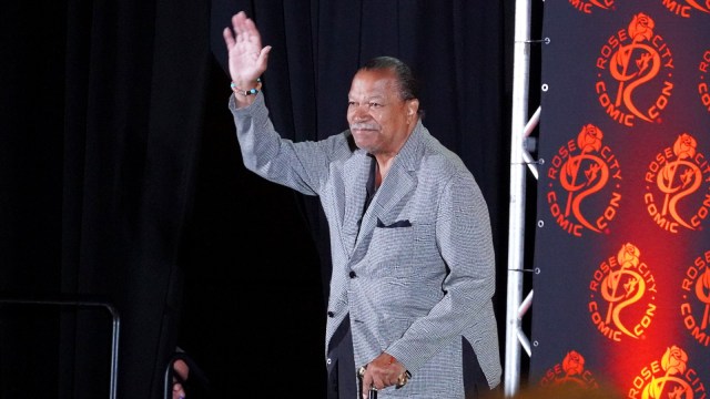 Billy Dee Williams waves at fans at a comic book convention panel.