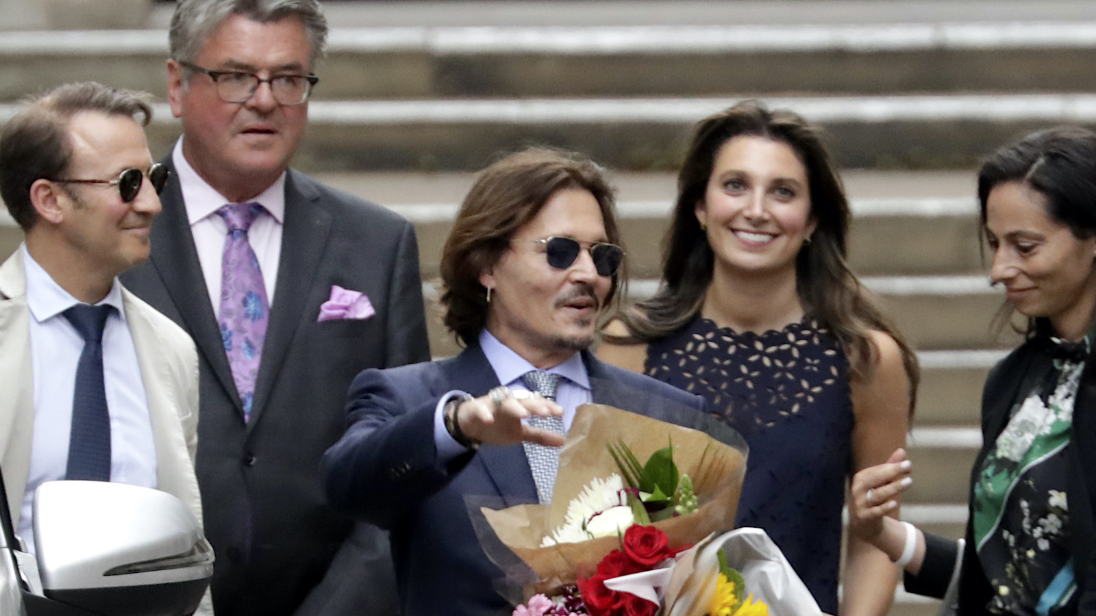 Johnny Depp outside courthouse of U.K. defamation trial, holding a bouqet of flowers. Joelle Rich stands behind him