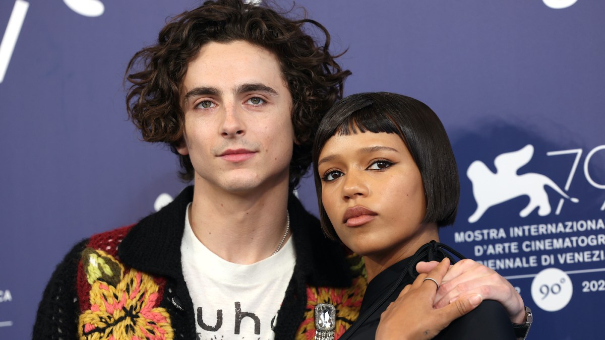 (L) Timothée Chalamet sports signature curly hair on the red carpet for 'Bones and All' at 79th Venice International Film Festival. His arm is wrapped around costar (R) Taylor Russell whose straight hair rests above her shoulders.