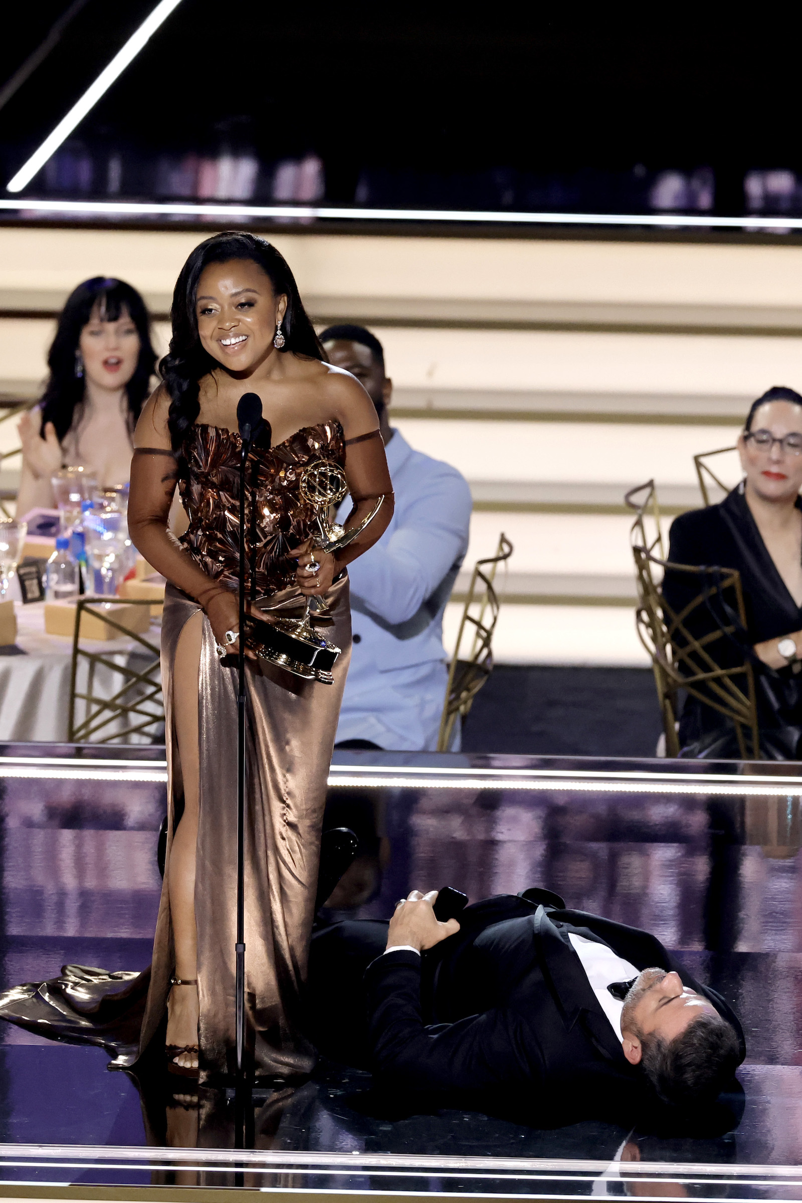 Quinta Brunson accepts Outstanding Writing for a Comedy Series for "Abbott Elementary" while Jimmy Kimmel lies onstage during the 74th Primetime Emmys at Microsoft Theater on September 12, 2022 in Los Angeles, California.