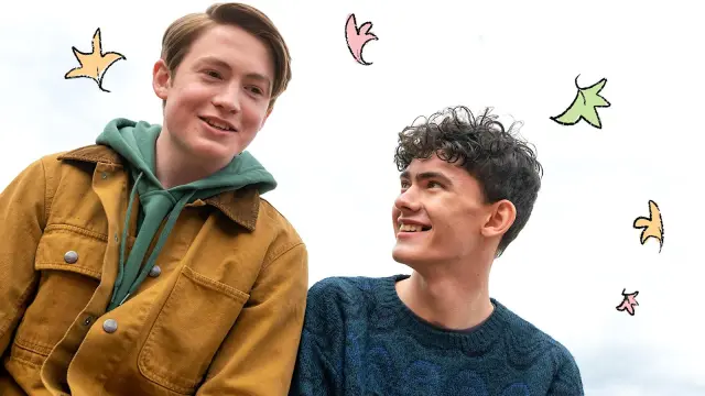 Promotional photo of Joe Locke and Kit Connor as Charlie and Nick in 'Heartstopper." Charlie looking up at Nick, smiling, cartoon leaves floating around them