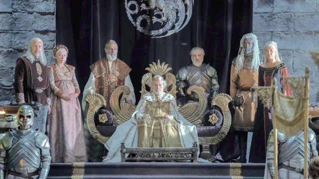 King Jaehaerys sits on his throne flanked on either side by members of the royal court and family.