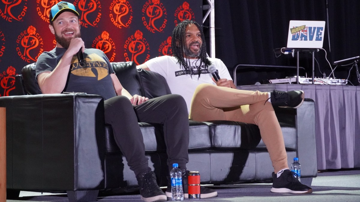 Khary Payton and Ross Marquand field fan questions from a couch on a stage at a Comic Con panel in casual dress.