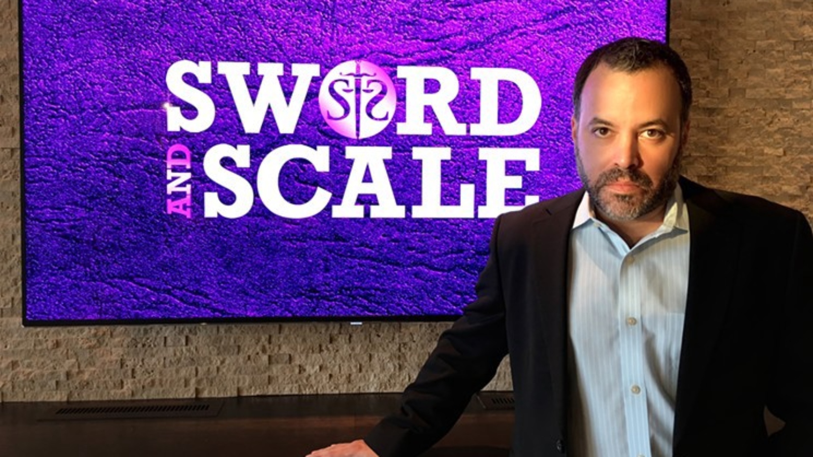 Mike Boudet standing in front of a Sword and Scale logo
