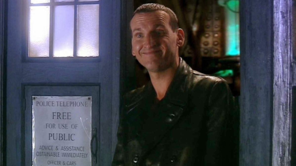 Christopher Eccleston's Ninth Doctor grins while standing in the TARDIS doorway in Doctor Who