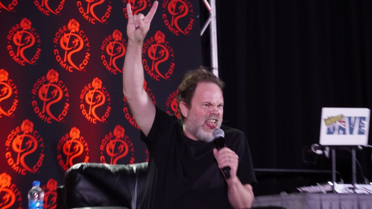 Rainn Wilson throws up a rock 'n' roll salute and sticks out his tongue at a comic con panel.
