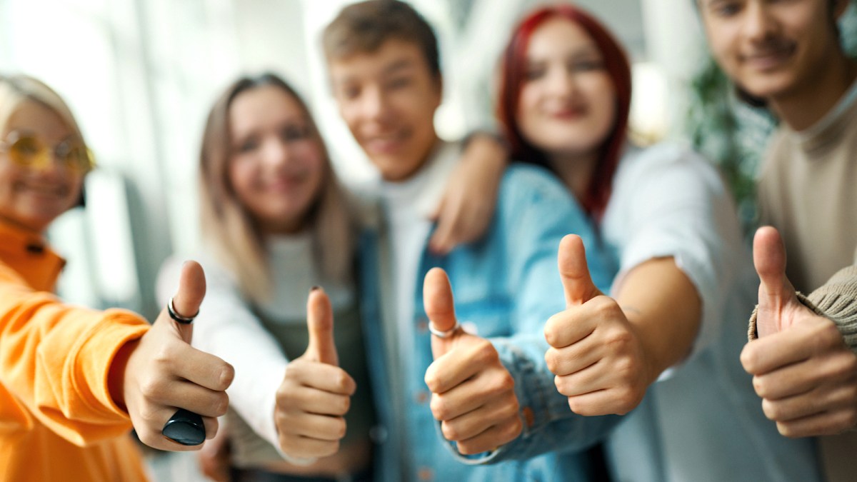 Closeup front of a group of high school students on a break between classes showing thumbs up to the camera.