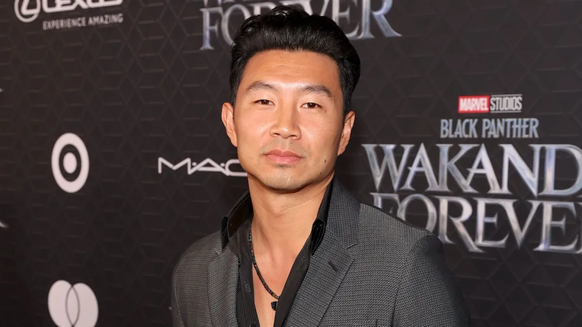 Simu Liu on the red carpet sporting an open necked black button down and a grey blazer