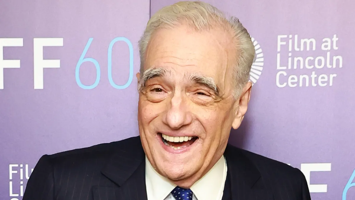 Martin Scorsese flashes a smile wearing a three-piece suit at a red carpet event.