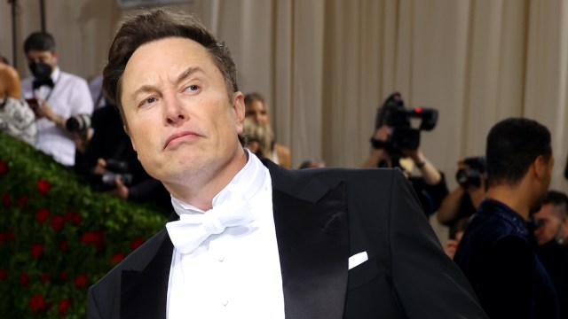 Elon Musk wearing a black and white suit on the red carpet and sporting a confused face.