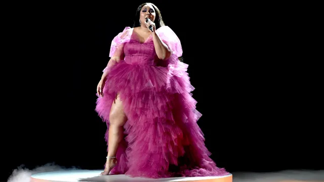 Lizzo sings on a stage while wearing a purple dress.