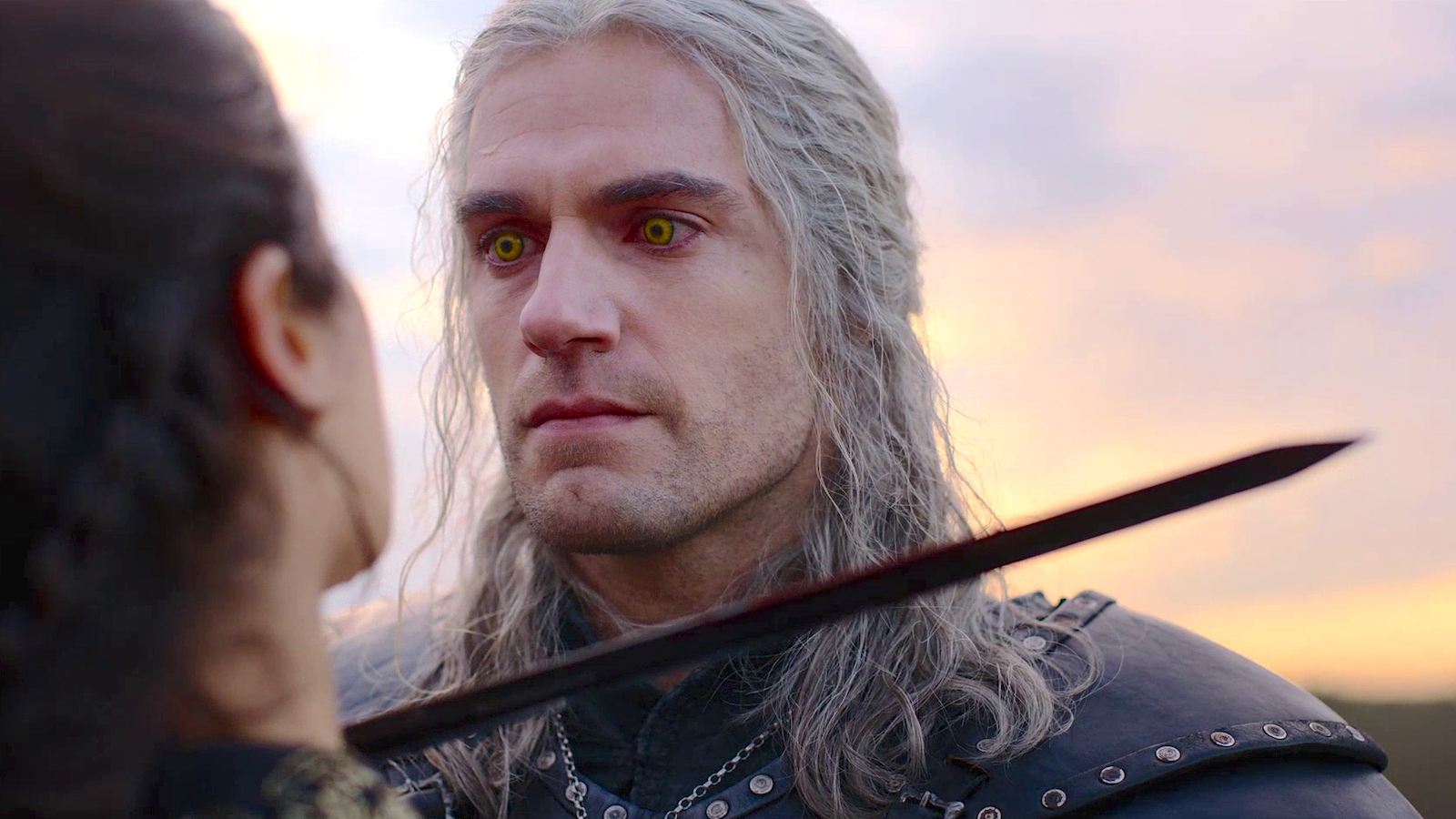 Geralt of Rivia (Henry Cavill) holding a sword to the neck of an unseen women, glaring at her with yellow eyes