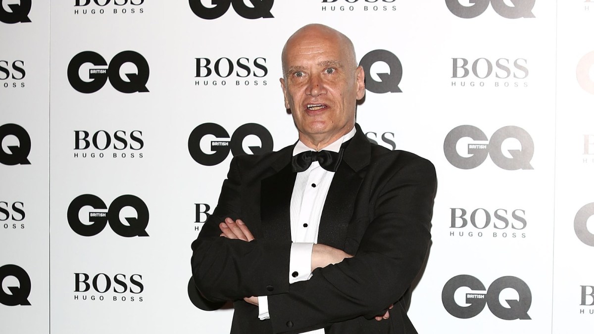 Wilko Johnson strikes a pose while wearing a tuxedo at a red carpet event.