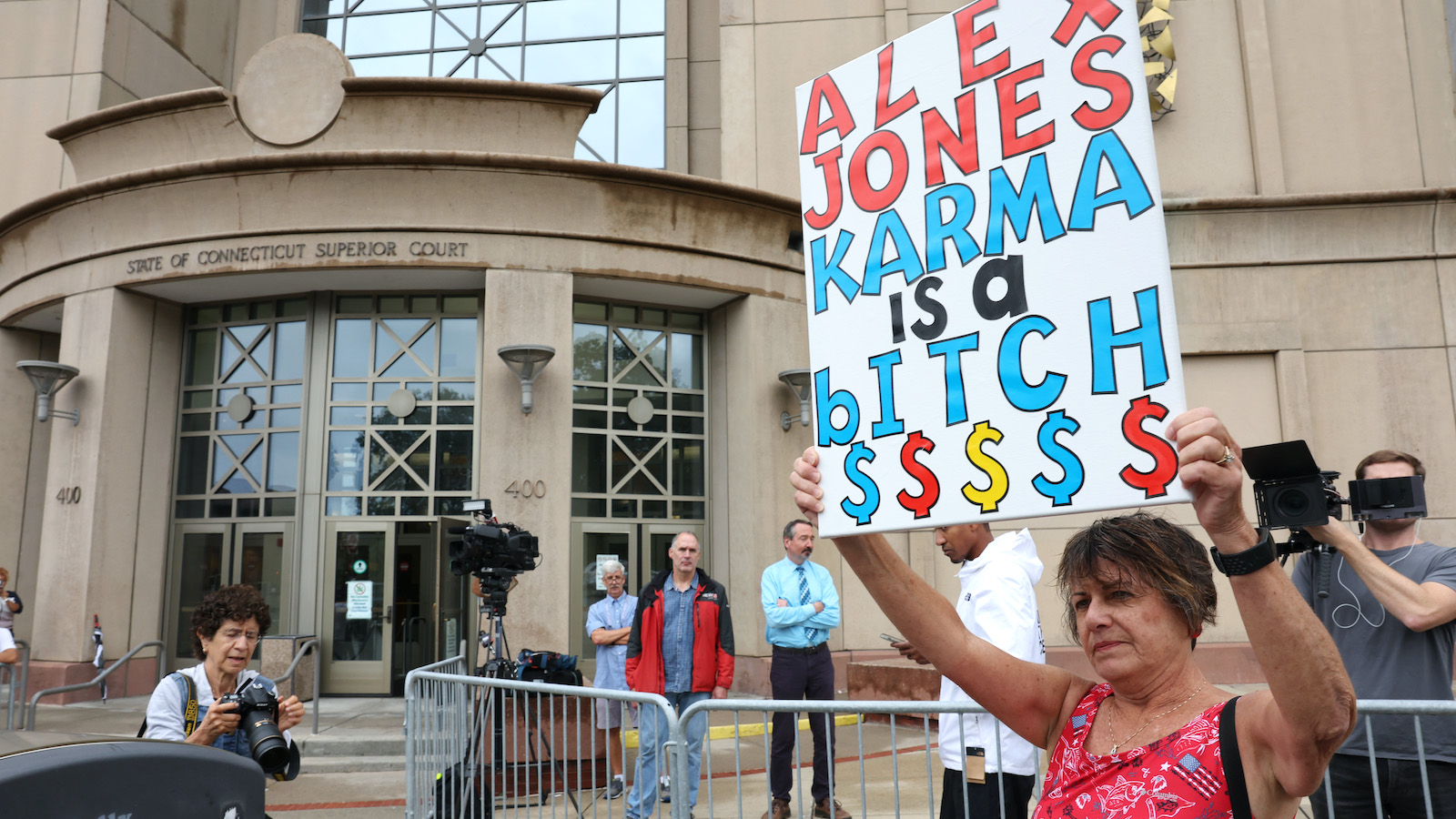 A lone protester standing outside the Waterbury Superior Court during the start of the trial against Alex Jones holding a sign that reads "Alex Jones Karma Is A Bitch"