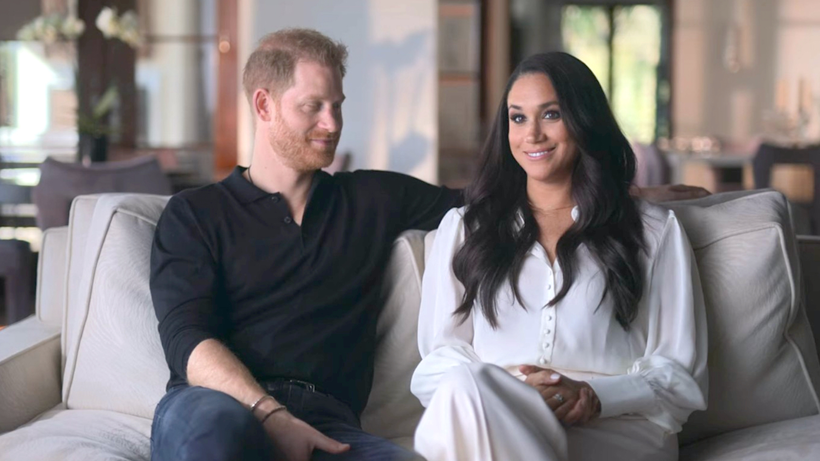 Prince Harry sitting beside wife, Meghan Markle on a sofa