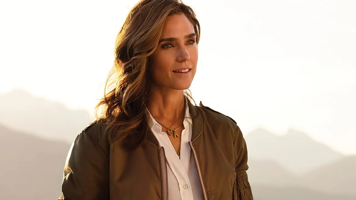 Jennifer Connelly's Penny gives a loving gaze while wearing a pilot's jacket and set against the backdrop of mountains in the distance. 