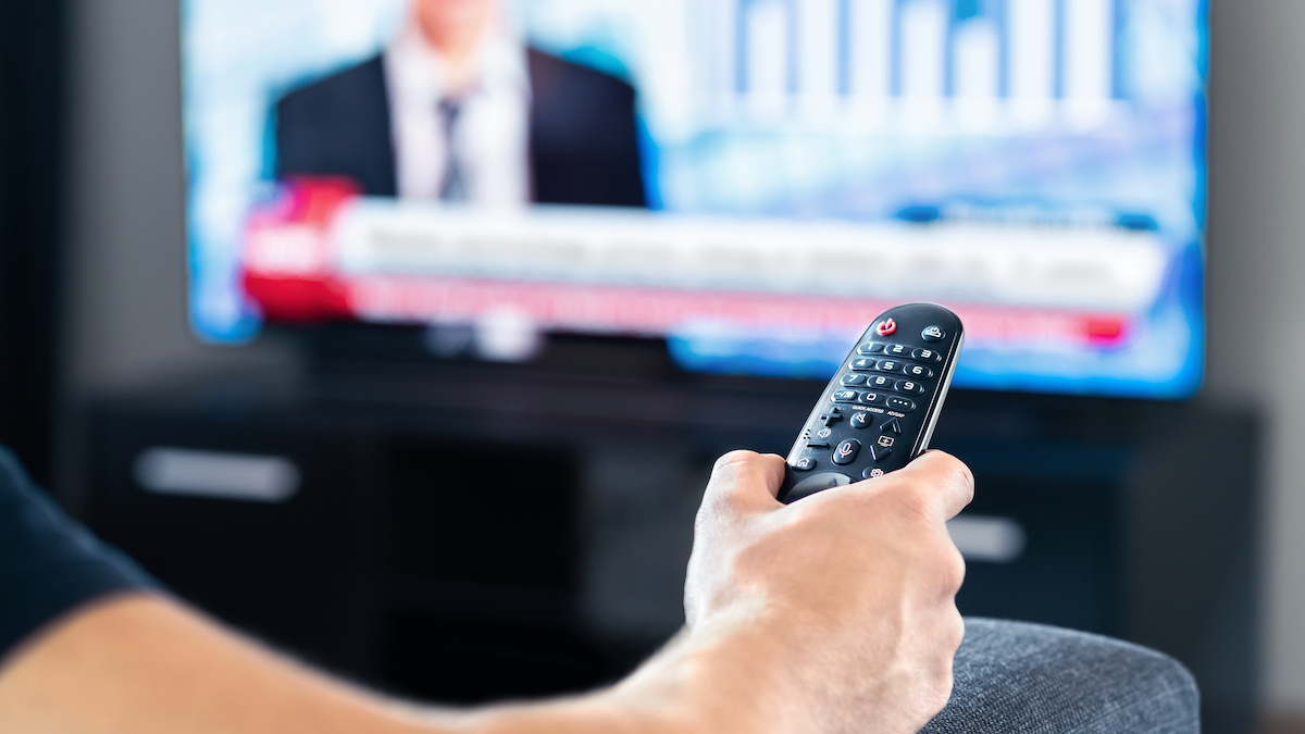 Man watching tv news program and sitting on couch home. Television remote control in hand. Politics, business or finance network channel. Online live broadcast in monitor screen. Morning newscast.