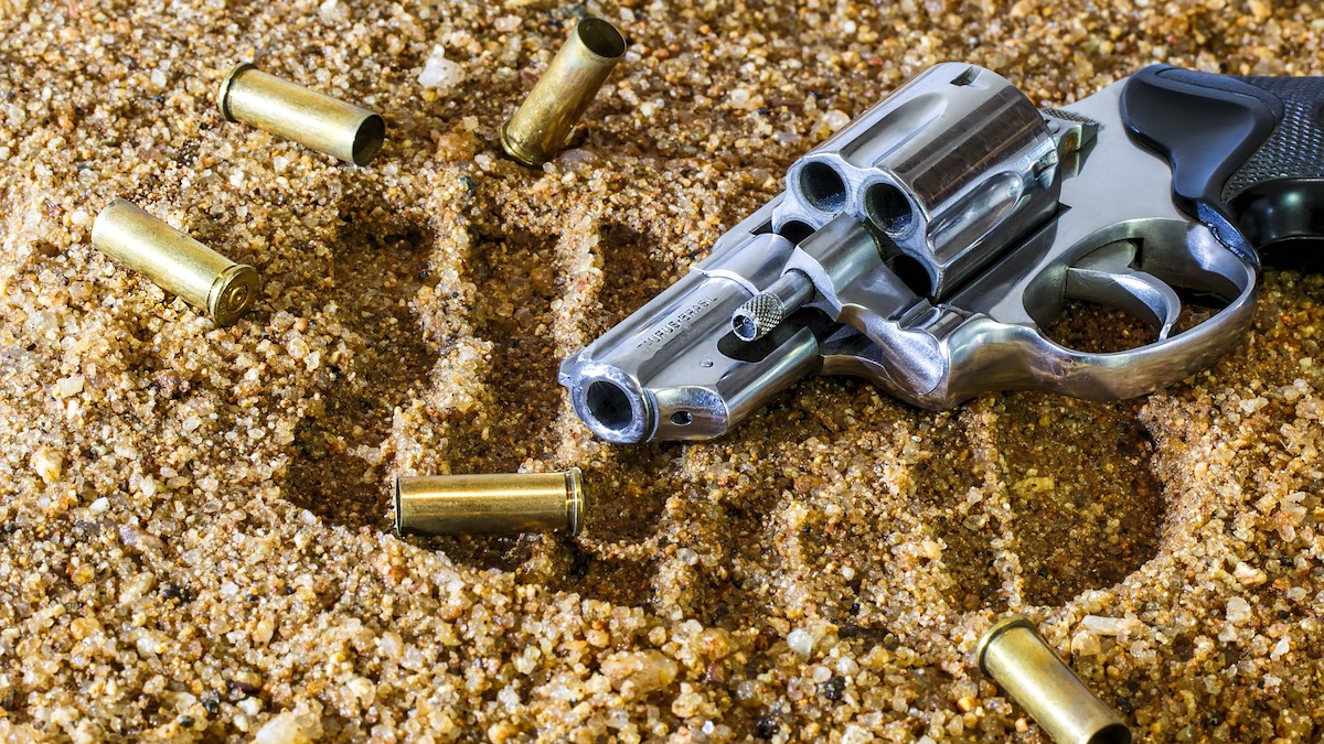 Image of a gun with lying in sand with blank bullets surrounding it 