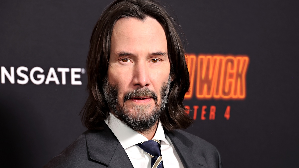 Keanu Reeves wearing a white shirt, grey suit, and tie on the red carpet of John Wick premiere
