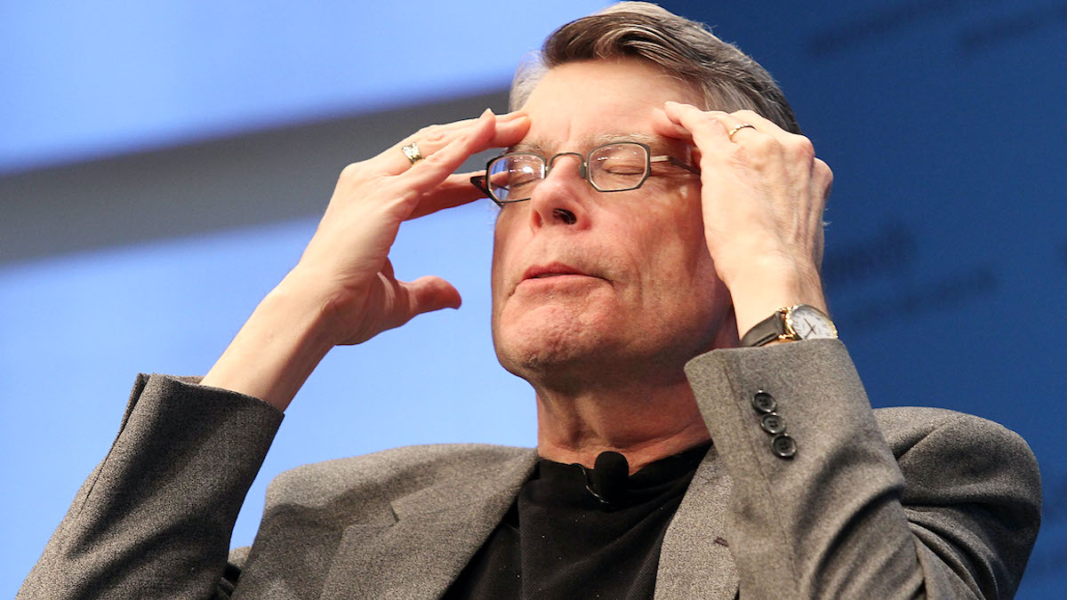 Stephen King with his eyes closed, head tilted back, and forefingers pressed to his temple in apparent frustration