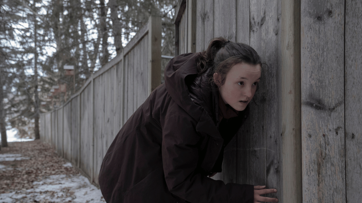Ellie (Bella Ramsey) sneaking along a fence line
