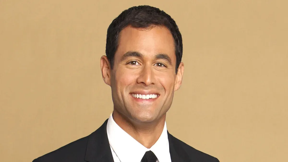 Jason Mesnick from season 13 of The Bachelor is smiling and standing in front of a yellow background.