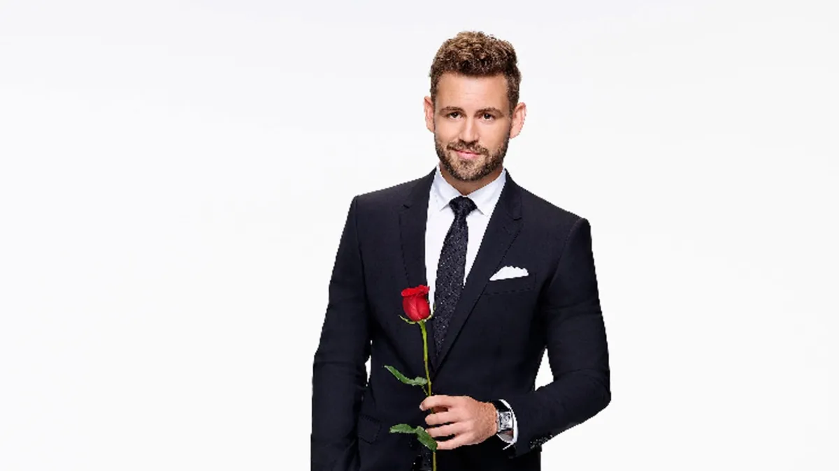 Nick Viall is holding a rose and looking at the camera.