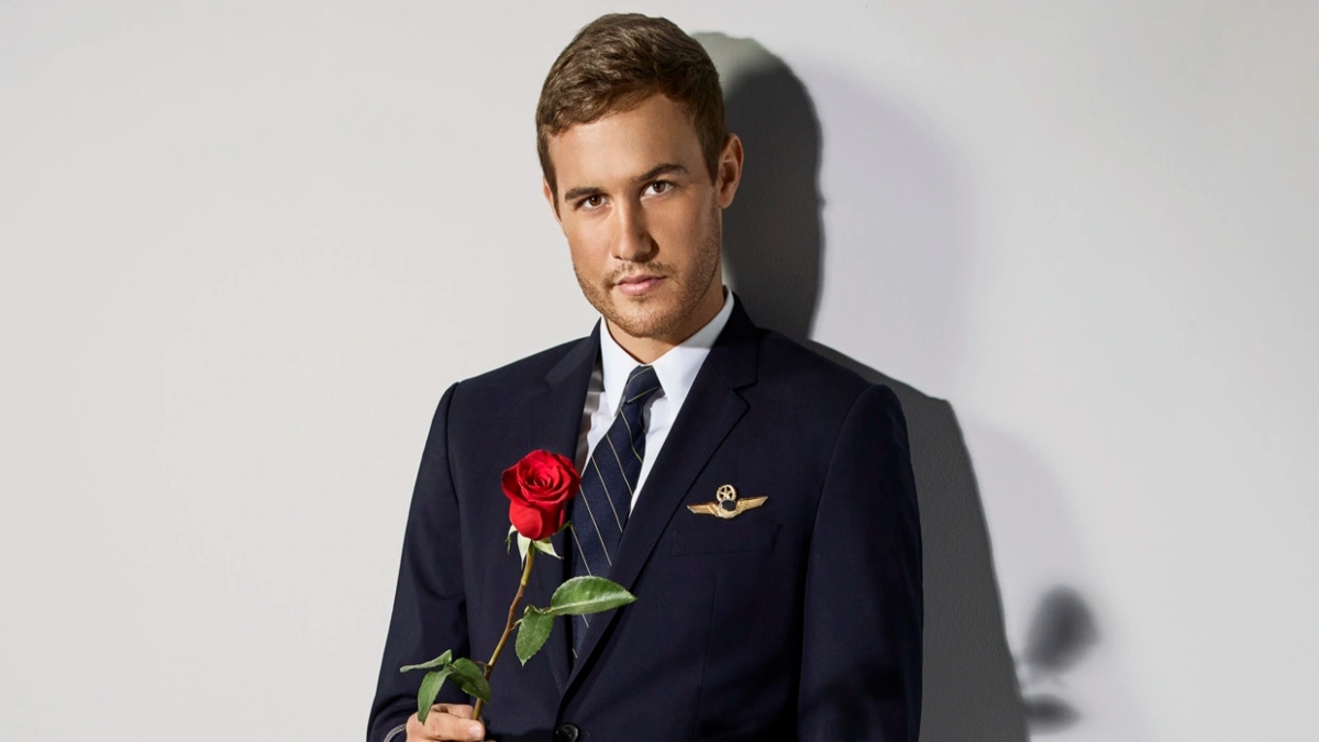 Peter Weber is holding a rose in his pilot uniform.